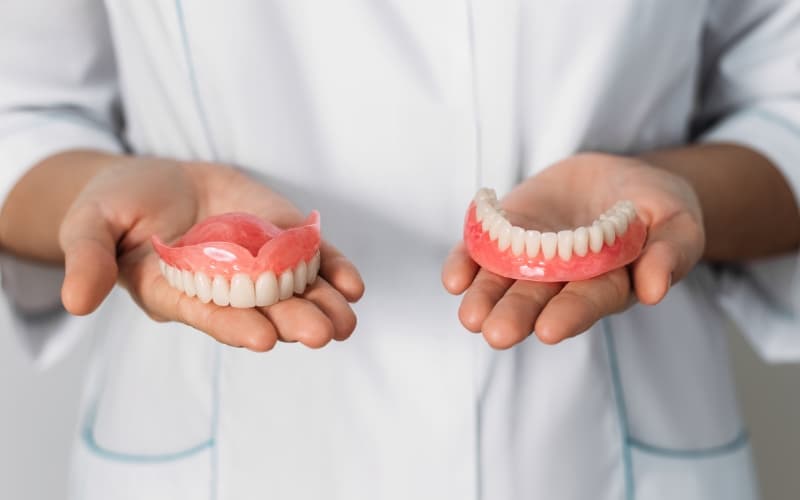 A full set of upper and lower dentures held in a clinician's hands