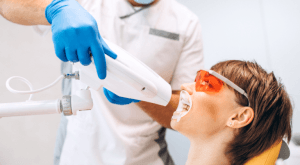 A patient in protective eyewear undergoing professional teeth whitening with a whitening lamp