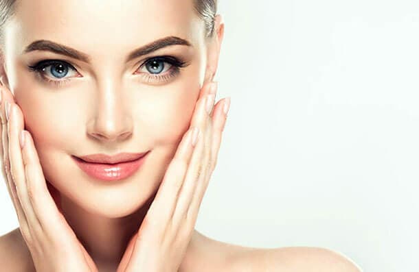 A woman with clear, even skin resting her hands against her face