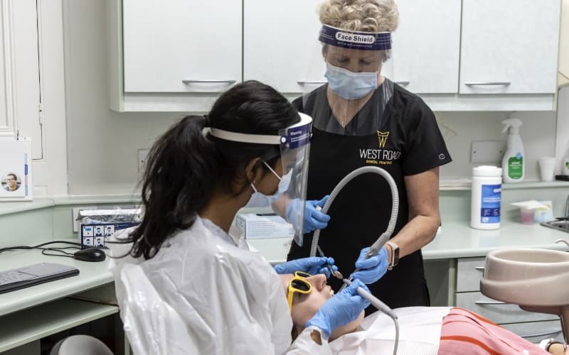 Two clinicians in protective visors and scrubs treating a patient in the surgery