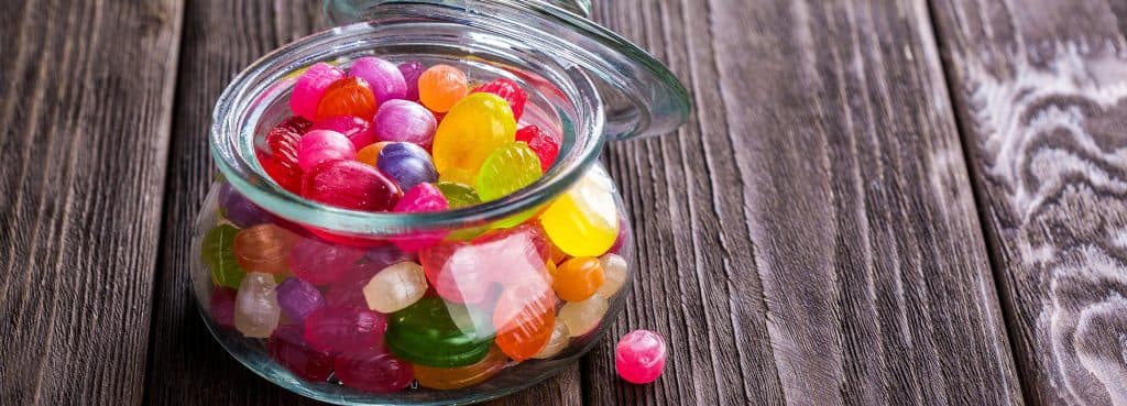 A glass jar of brightly coloured sweets on a wooden table